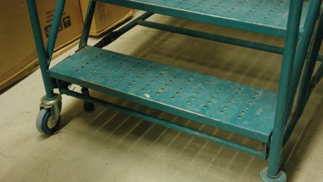 worker unlocks the latch of a blue industrial rolling staircase in a warehouse