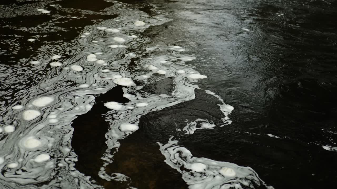 burbujas de espuma que flotan en la superficie del agua oscura en el río north esk en escocia se arremolinan juntas para formar un patrón en constante cambio donde la corriente más rápida se encuentra con una sección de agua inmóvil