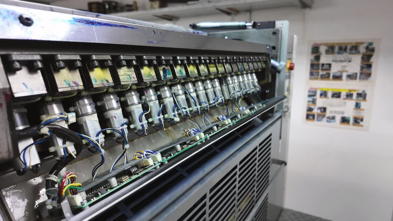 Industrial printing machine with a downward tilt, close-up of ink injectors on the panel.