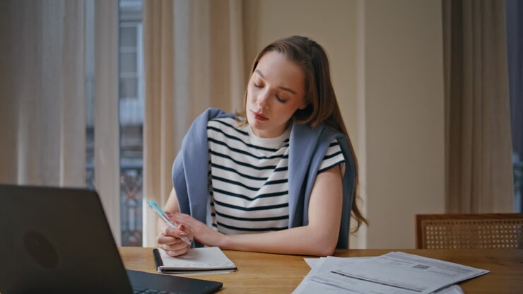 Kvinnelig lærer som snakker i en online leksjon og noterer i notatbok hjemme nærbilde