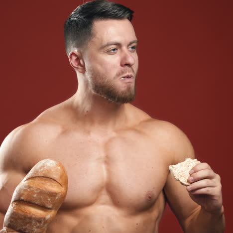 portrait of bodybuilder eating healthy food. sportsman choosing special bread important for his strong body. red studio background. healthy food choices.