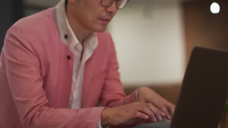 Elegant-Gekleideter-Asiatischer-Geschäftsmann,-Der-Mit-Laptop-Am-Schreibtisch-Sitzt-Und-Sich-Wundert