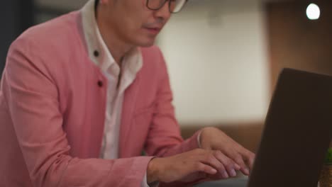 ⁇ 하게 옷을 입은 아시아 비즈니스맨이 책상에 앉아 노트북을 사용하고 있습니다.