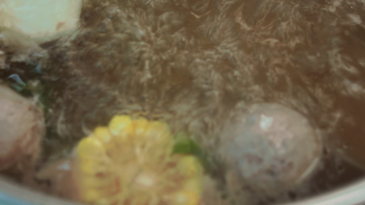 Bubbling pot boiling corn and carrots with steam swirls, cooking process close-up.