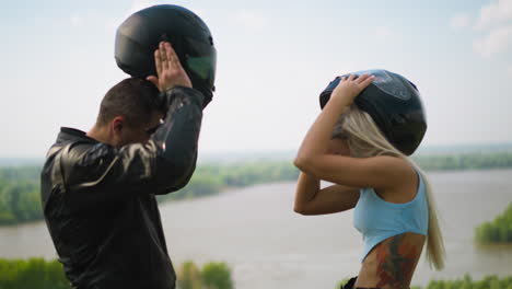 man and woman take off moto helmets against large lake