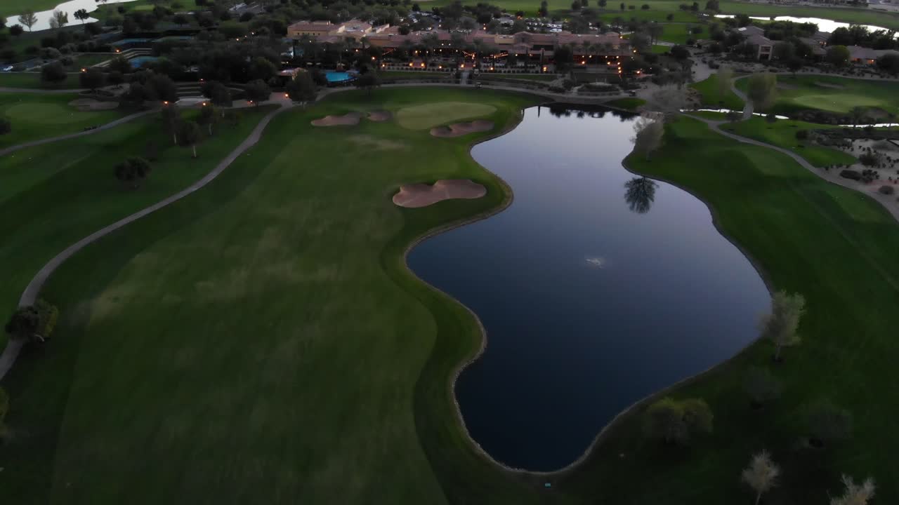 Drone footage from a golf course near a residential neighborhood in Arizona. High aerial shot of the greens, fairway and water hazard