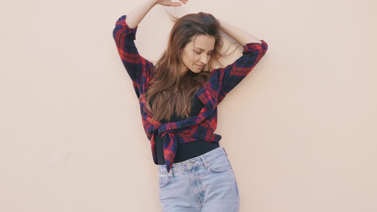 mujer con una camisa a cuadros y vaqueros posando frente a una pared de color beige claro