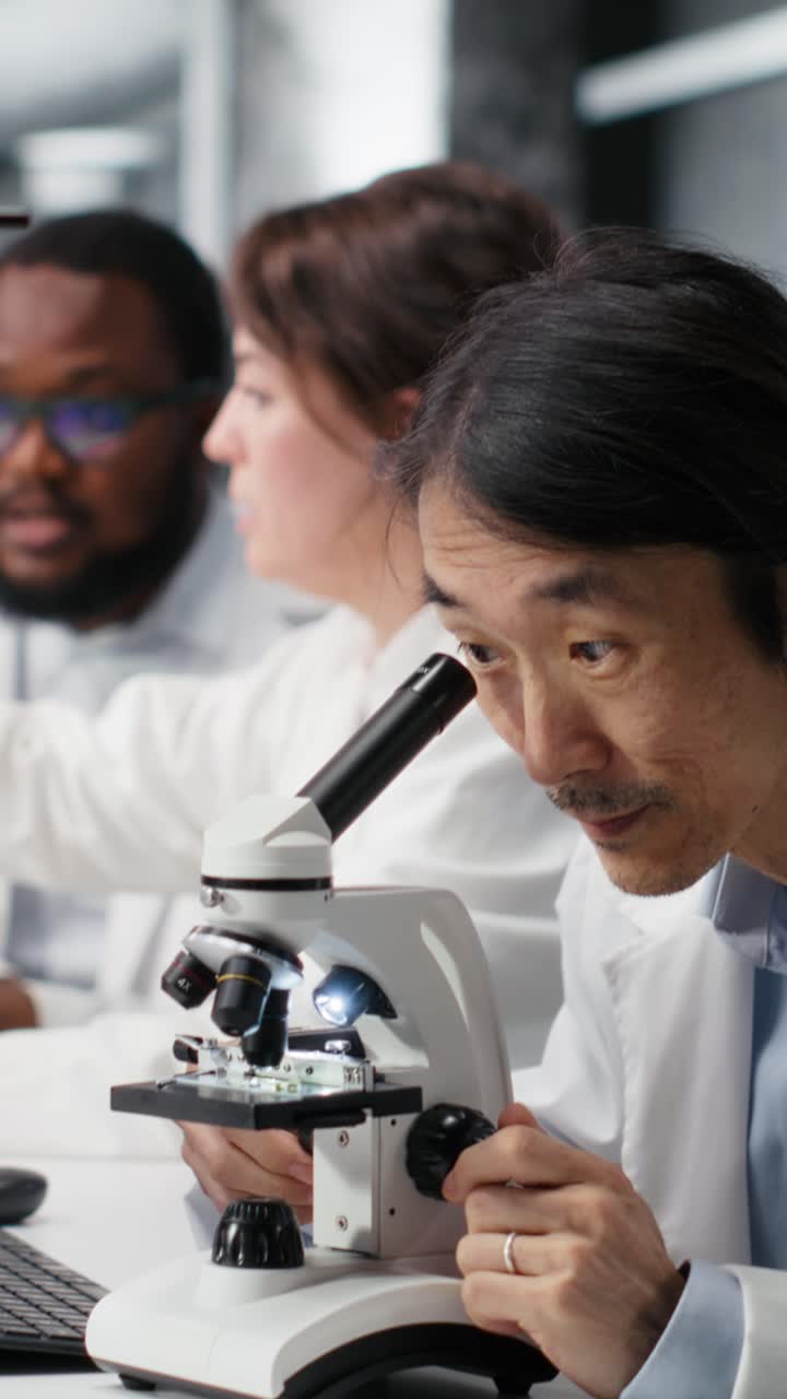 Vertical video Team leader writes down observations for lab coworkers using microscope