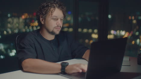 curly-haired man works at a computer at night