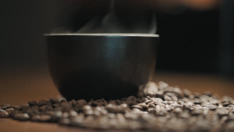 steam over a cup of coffee on a wooden table surrounded by fresh coffee beans slow motion