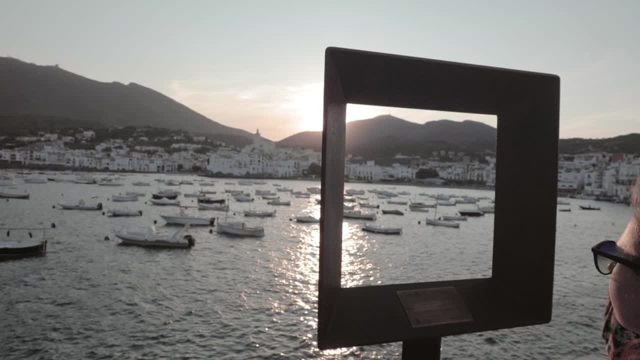 unidentified woman looks at ships in the water from behind a glass frame in Roses, Costa Brava, Catalonia, Spain