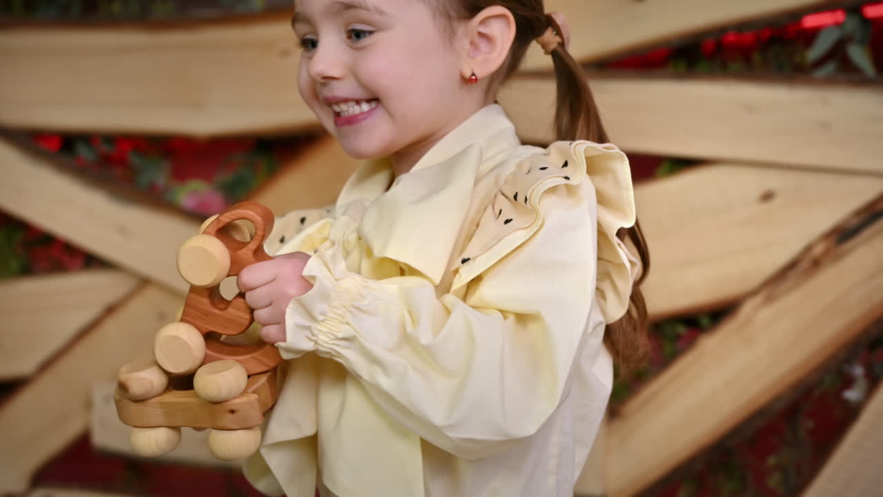 Little girl with blue eyes holding two wooden snail rolling toys and smiles. Ecological and sustainability concept