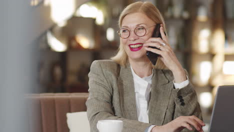 senior businesswoman speaking on phone and using laptop in restaurant