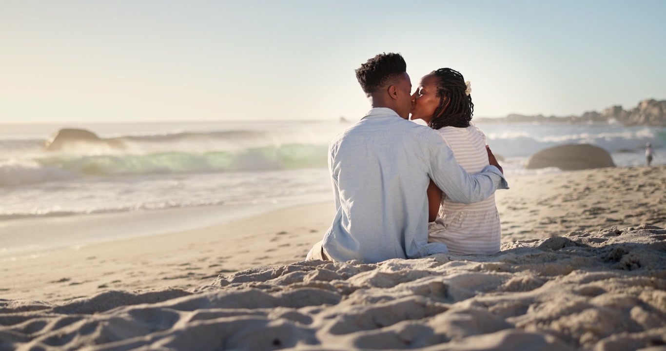 Young Couple Sitting and Kissing on the Beach at Sunset