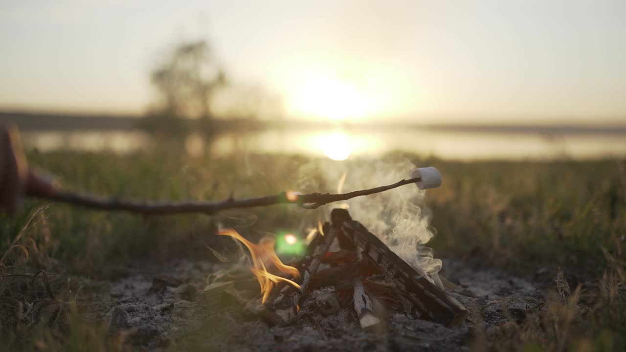 해가 지는 해변에서 불꽃 위에 마쉬멜로를 구워