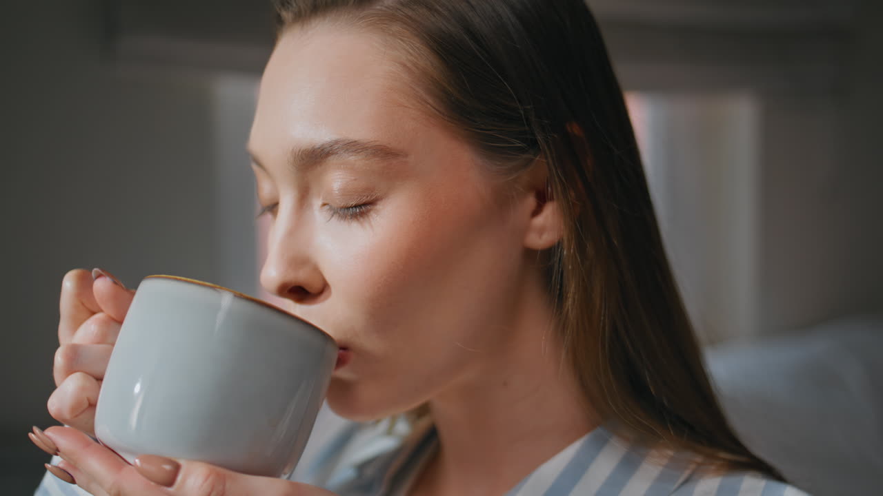 Relaxed girl sipping coffee in bedroom starting morning with smile closeup