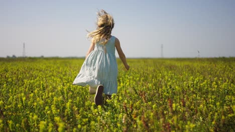 Young-girl-in-summer-dress-runs-through-meadow-covered-in-yellow-flowers,-slomo