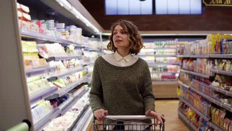 Portrait-of-happy,-relaxful-woman-with-curly-hair-went-shopping-with-trolley-cart---walk-by-a-row-and-happily-dancing-in