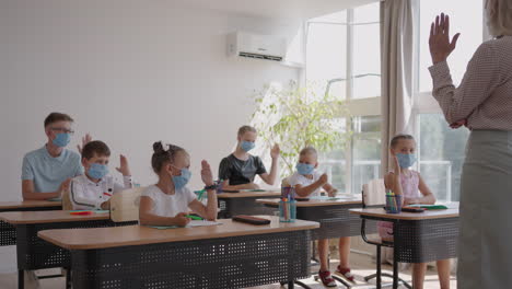 raise your hand to answer the teacher's question. multi-ethnic group of children with face masks at school during covid-19 pandemic.