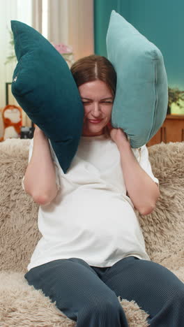 Pregnant woman tries relaxing but neighbors knock sofa shows stop gesture covers ears with pillows