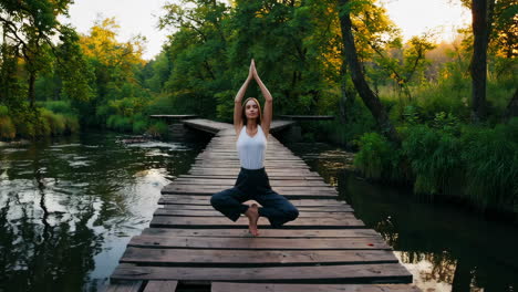 woman practicing yoga and meditating on a wooden bridge over a river in a serene natural setting