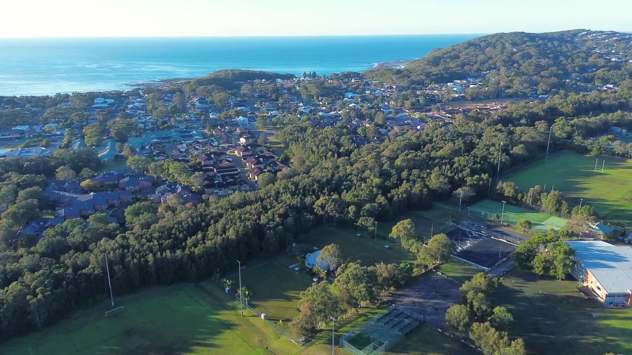 Paesaggio aereo ripreso da drone di un quartiere residenziale con case e campi sportivi pubblici circondati da alberi della boscaglia rurale e strade costiere a Bateau Bay, Central Coast Australia, infrastrutture e turismo.
