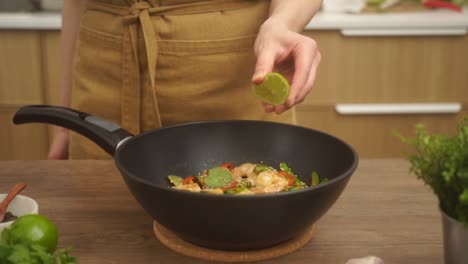 crop faceless woman adding lime juice to stir fried prawns