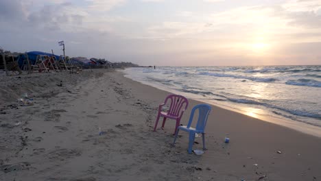 Zwei-Einsame-Plastikstühle,-Die-Inmitten-Der-Verwüstung-Des-Krieges-In-Gaza-Am-Strand-Zurückgelassen-Wurden