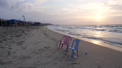 dos sillas de plástico abandonadas en la playa entre la devastación de la guerra en gaza