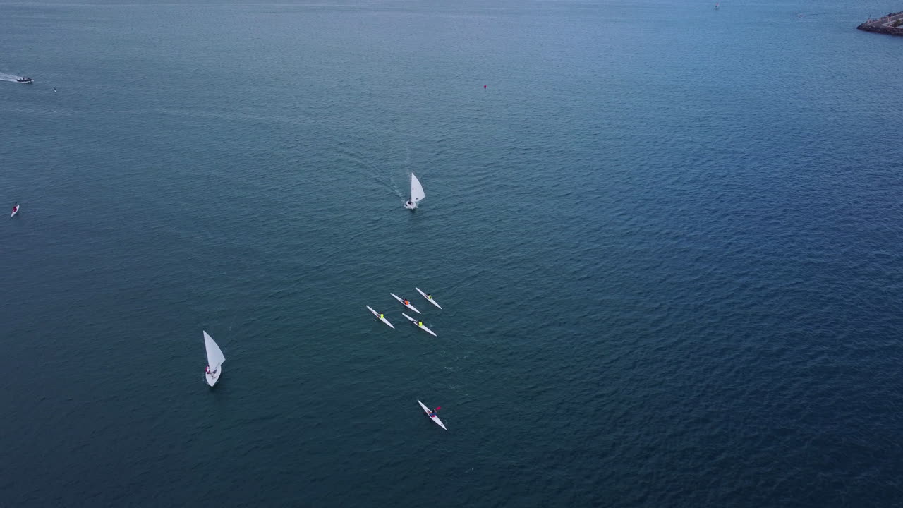 toma aérea sobre el agua, veleros y botes de esquí de surf, muelle a la izquierda y puerto en el horizonte