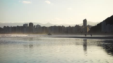 surfers walk on the sand towards sea at dusk