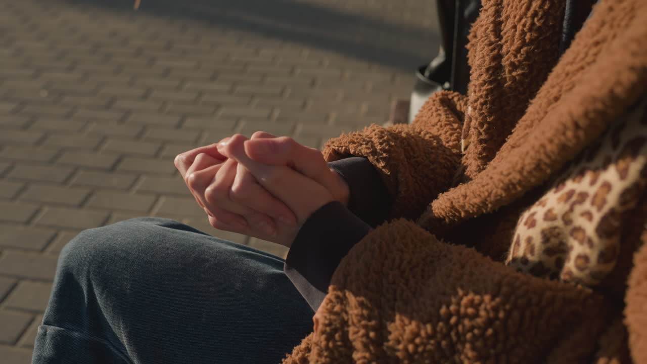 얼굴이 보이지 않고, 파란 청바지와 갈색 코트를 입고, 손을 접고 서로 마시고 앉아있는 사람의 클로즈업.