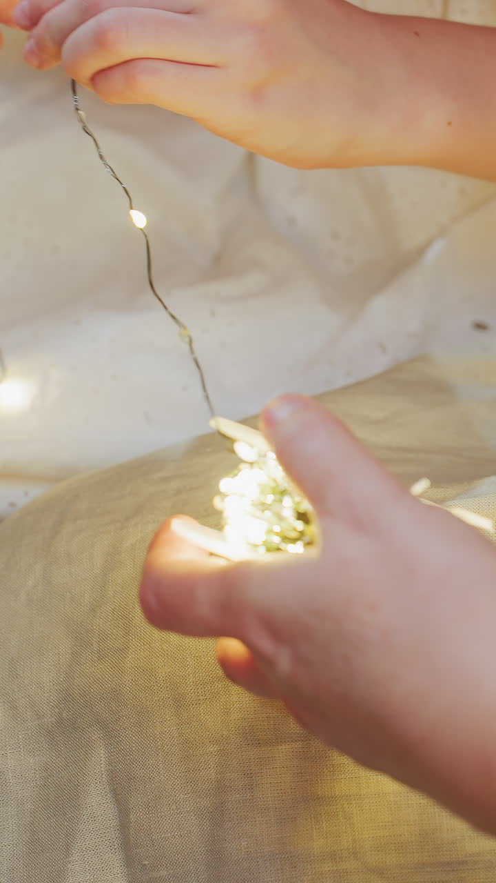 요정 불빛을 감싸 쥔 손, 부드러운 리넨 위에 따뜻한 끈을 조심스럽게 풀고 있는 어른의 모습, 황금빛의 클로즈업, 섬세하게 감싸는 동작, 아늑한 침실 분위기, 장식 공예