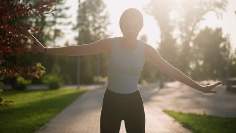 young lady smiling while skating outdoors with hands wide open for balance, sunlight reflecting off her creating bright glow, and blurred background of lush greenery, trees, and natural park scenery