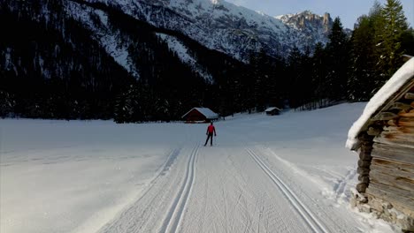 person in red dress skiing on snowy terrain between wooden houses