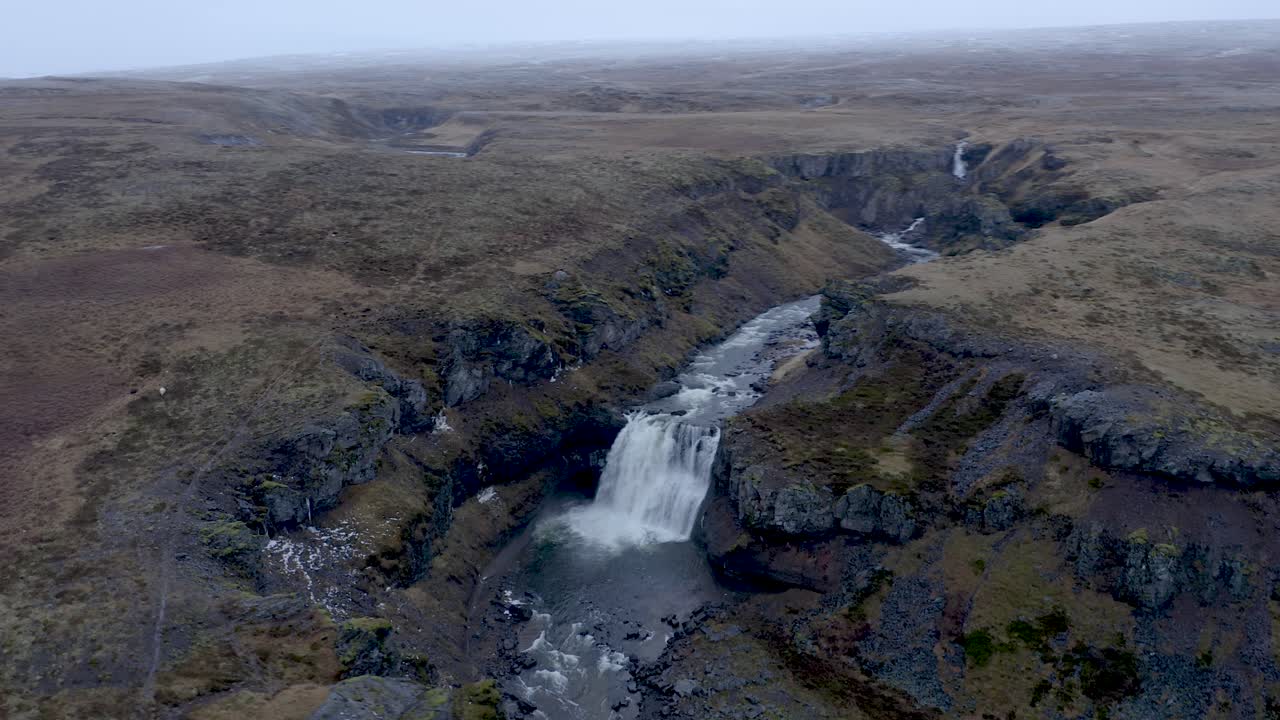 impresionante toma aérea circular de una cascada que cae en el río selá rodeada de colinas durante el día nublado - norte de islandia en la temporada de otoño