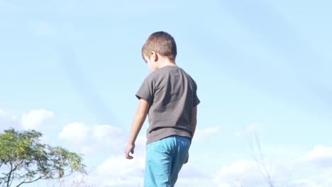niño pequeño caucásico mirando el suelo y de pie caminando, vista a nivel del suelo bajo, con un hermoso cielo azul en el fondo 120fps