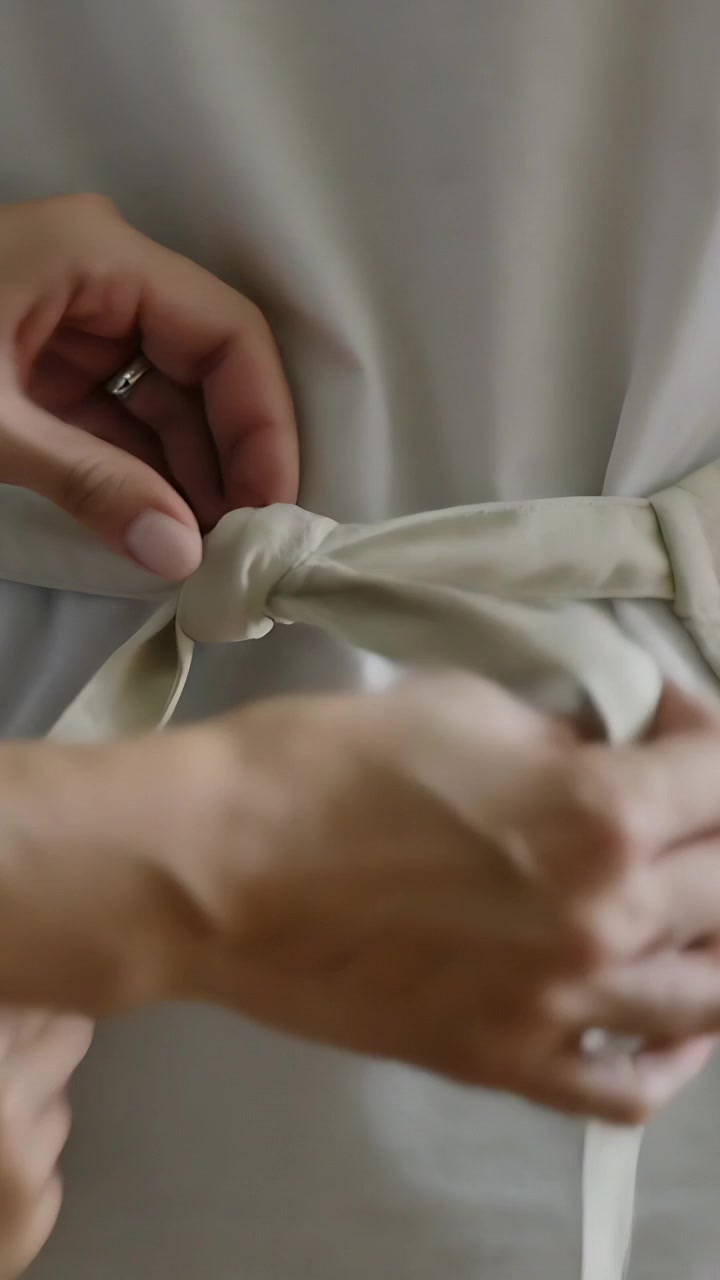 Vertical video: Reaching helper tying sash around adult waist at home, securing shirt and jeans
