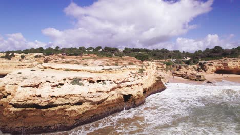 Vista-De-La-Costa-Con-Cala-De-Playa-En-Transición-A-Acantilados-Escarpados-De-Color-Naranja-Con-Grupos-De-Excursionistas-Y-Un-Arco-Natural-Tallado-Por-Un-Dron-Aéreo-4k-En-La-Playa-De-Albandeira-En-La-Región-Del-Algarve-De-Portugal