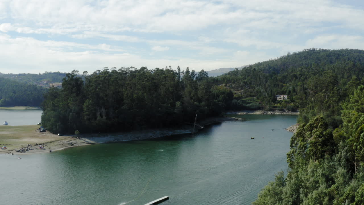 árboles frondosos en una pequeña isla rodeada de agua de lago oscuro en vieira do minho, portugal en un día soleado - disparo ascendente de drones