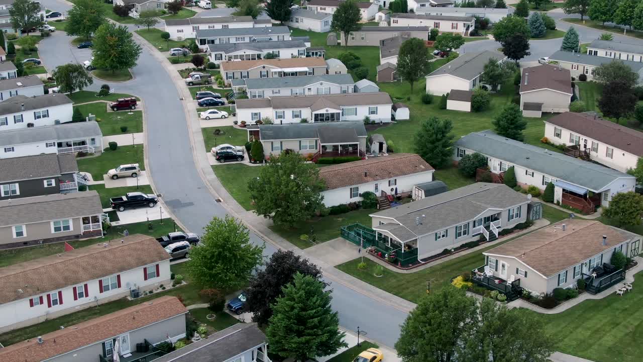 Mobile home park, prefab manufactured houses, single-story trailer park neighborhood community, rising aerial view, United States of America, USA, daytime summer shot with green lawns