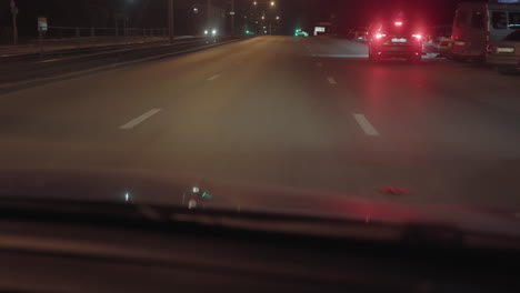 car driving through quiet street at night with headlights and tail lights from multiple vehicles visible, deserted road under glow of street lamps