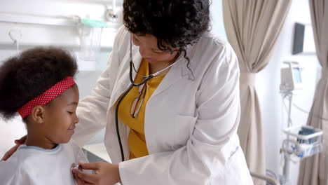 african american female doctor examining girl using stethoscope in hospital room, slow motion