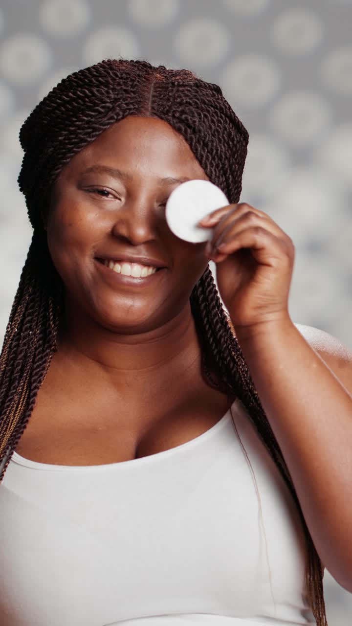 Vertical video: Smiling woman posing with cotton pads in studio