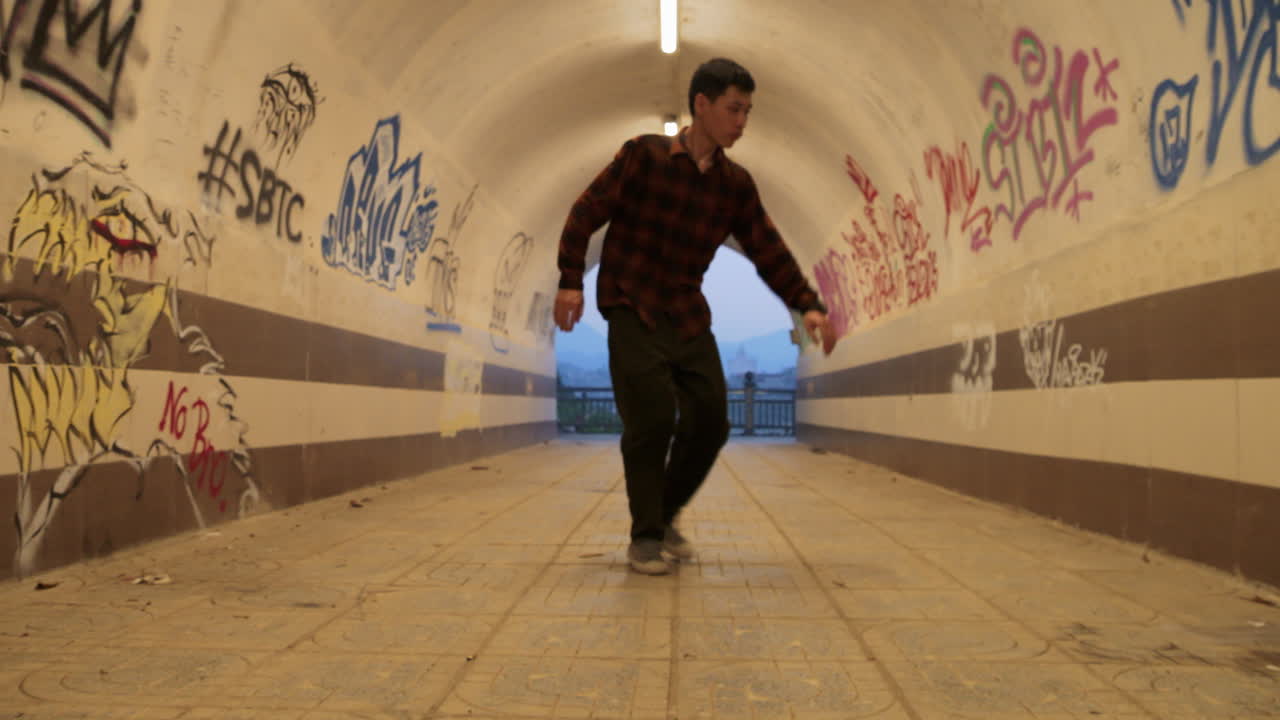 hombre asiático experto bailando estilo libre urbano en un túnel callejero con graffiti