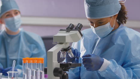 female lab workers wearing ppe analysing samples in laboratory with microscope record test results