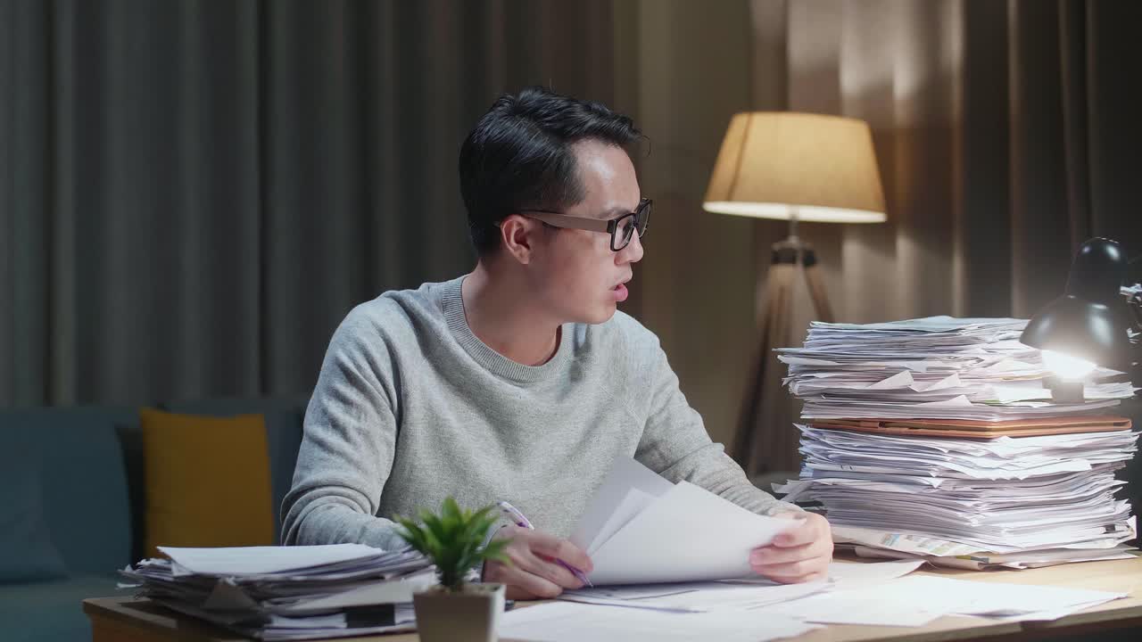 Tired Asian Man Yawning And Sleeping While Working Hard With Documents At Home