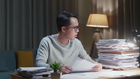 tired asian man yawning and sleeping while working hard with documents at home