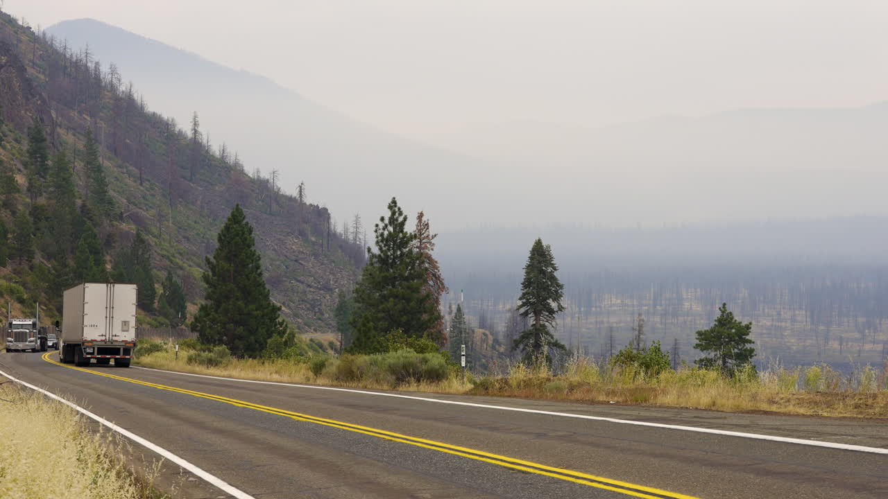 White Semi-Truck Driving on a Hazy Mountain Highway Through Burnt Forests