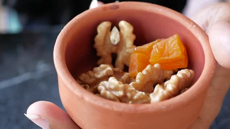 hand picking dried apricots and walnuts from a small terracotta bowl